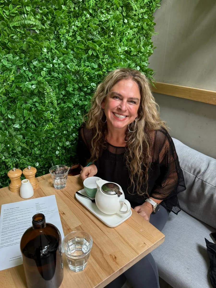 Dr Rebecca Chabot seated at a cafe table in front of a green living wall